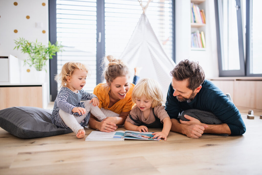 family with young children on laminate floor reading a book