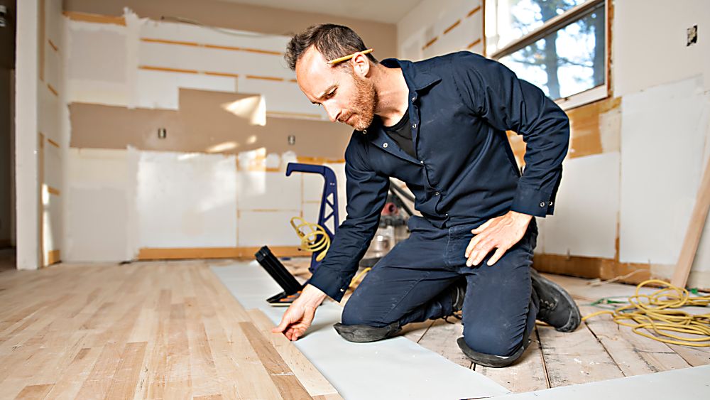 Hardwood flooring installation in a residential room with a contractor working on the floor